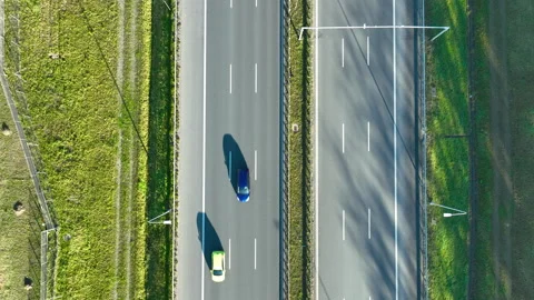 Top‑down drone view of two cars driving on parallel highway lanes with grassy Video stock 321859701