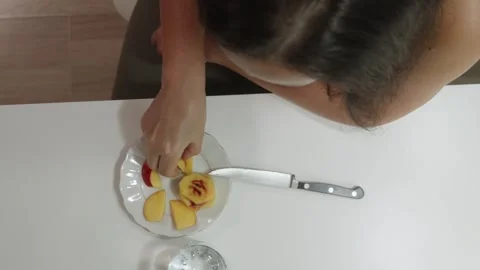 Topdown view of woman casually eating peach slices on clean table surface Stock Footage 331373853