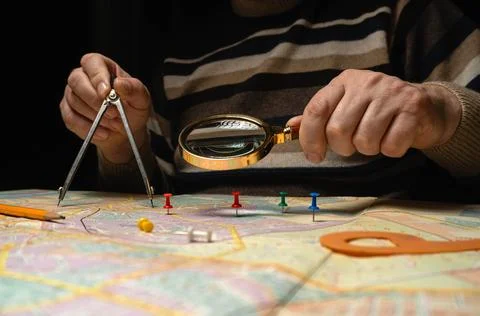 A topographer sits at a table and studies a map closely. They hold a compas.. 库存照片