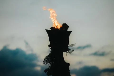 Torch with flame illuminated against a cloudy sky during twilight, showcasi.. Stock Photos