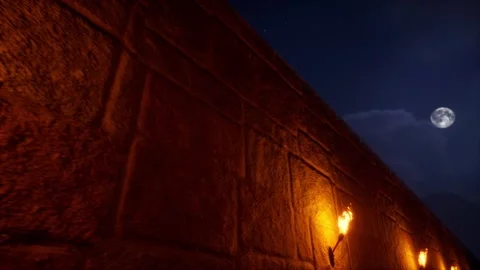 Torches burning on a stone wall and the moon shining over a hill in the back Stock Footage 283457057