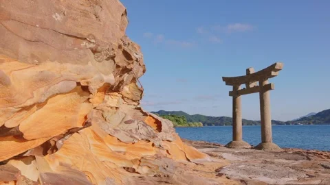 Torii gate standing by calm sea with unique sandstone rock cliff in foreground Video stock 340749739