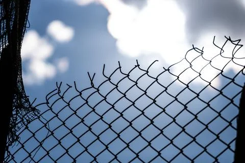 Torn and damaged upper edge of a metal wire mesh against a blue sky Foto stock