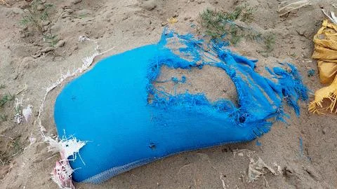 Torn Blue Woven Plastic Sack Lying Abandoned On Sand 库存照片