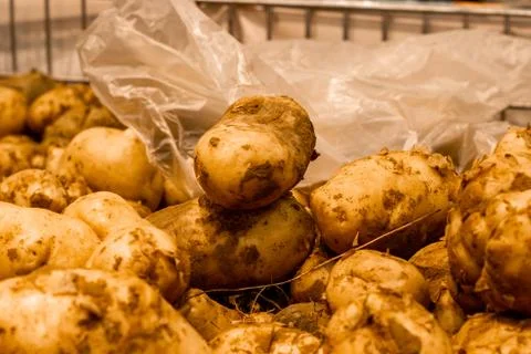 Torn plastic bag in a box with potatoes at the grocery store. Stock Photos