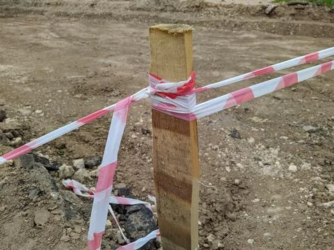 Torn red and white warning tape tied to a wooden support. Stock Photos