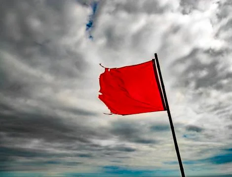 Torn, red warning flag flying under grey skies Stock Photos
