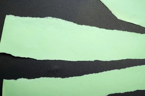 Torn strips of light green paper layered over a textured black glitter back.. Stock Photos