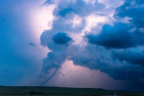 Tornado below a dark storm cloud illuminated by flashes of lightning Stock Photos