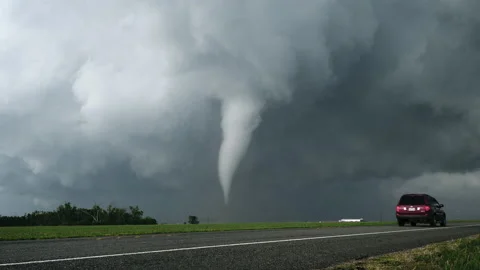 A Tornado Spins Over The Plains During Severe Weather As Cars Drive By Stock Footage 153499154