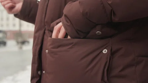 Torso close-up of person in brown padded jacket reaching into pocket while left Stock Footage 345652018