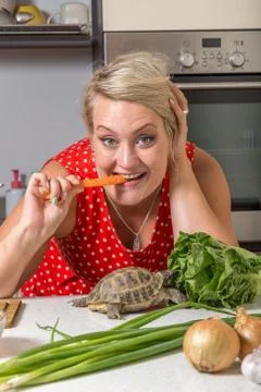Tortoise eating roman salad while young woman bites carrot Stock Photos