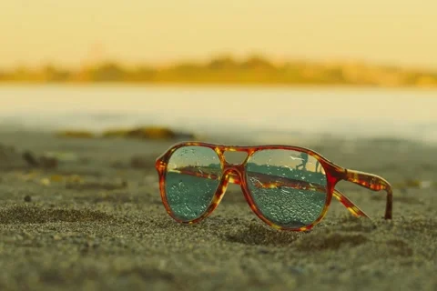 Tortoise shell aviator sunglasses with water drops on beach sand Stockbeeldmateriaal 332399593