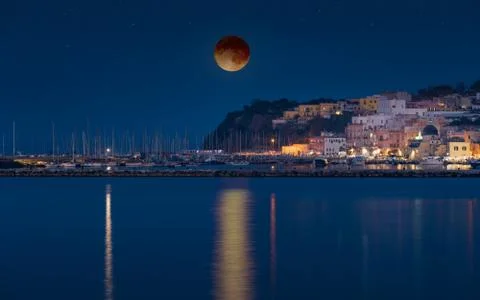 Total lunar eclipse above small seaside town Stock Photos