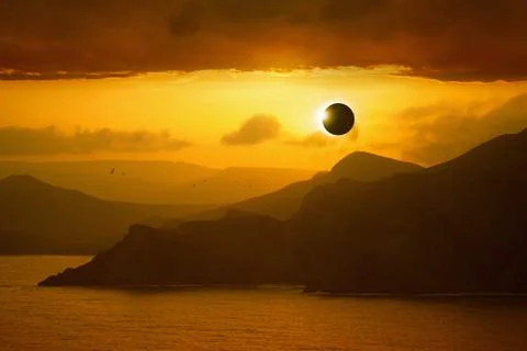 Total solar eclipse, silhouettes of mountains in red glowing sky 写真素材