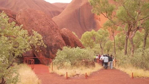Tour Group Gathering At Uluru Base Walk Entrance With Red Rock Cliffs And Stock Footage 336116905