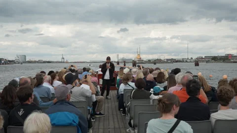 Tour guide points out landmarks to passengers on a harbor sightseeing cruise Stock Footage 345494539