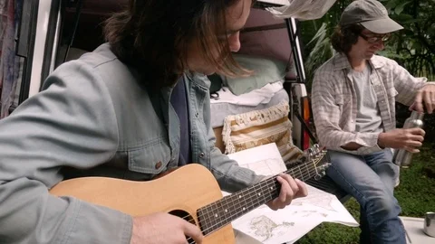 Touring musicians practicing guitar while camping on the road Stock Footage 80555423