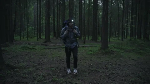 A tourist with a backpack and a head lamp slowly walks through the night forest 動画素材 201084344