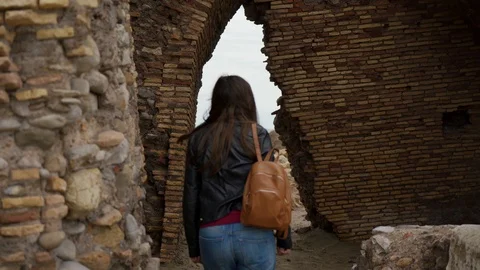 Tourist with backpack goes through arch in ruins of ancient fortress. Rear view 库存影片 123548587