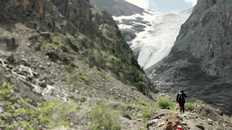 A tourist with a backpack on his back walks along a mountain path to a glacier. 스톡 동영상 281159907