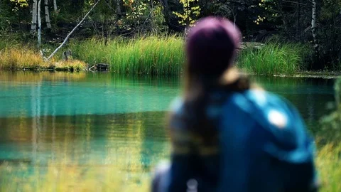 Tourist with backpack sits on a fallen tree by blue mountain lake. Lake is in 스톡 동영상 97408234