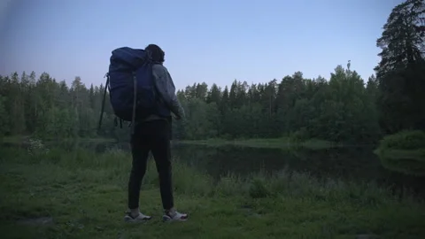 A tourist with a backpack slowly approaches the forest lake,stops,takes pictures 스톡 동영상 201083468