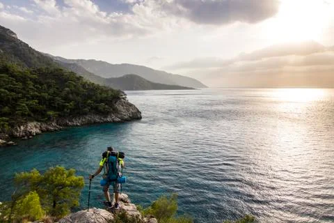 Tourist with backpack standing on a cliff in mountains near mediterranean sea Stock Photos