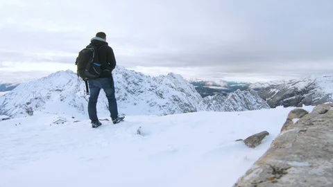 Tourist with backpack stands on mountain looking at snow covered landscape Stock Footage 100052685