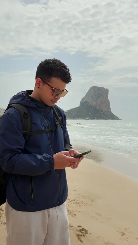 Tourist with a backpack using a smartphone to send text messages on the beach Stock-Footage 333690460