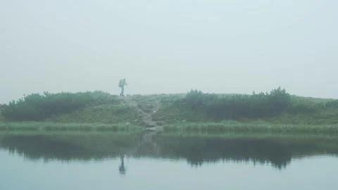 Tourist with a backpack walks against the background of a lake in foggy weather Stock Footage 214323445