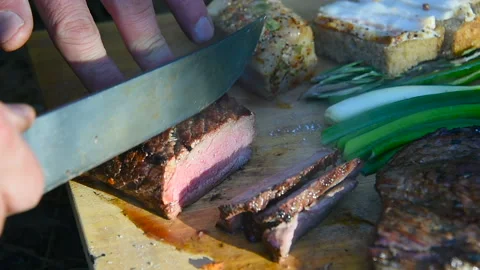 Tourist cuts fresh beef steak with a knife in a camping trip. Vidéo 101321423