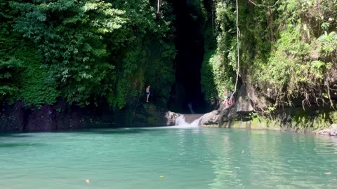 A tourist doing a rope swing jump into a hidden jungle lagoon in Bali Stock Footage 336904382