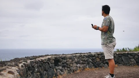 Tourist drives quadcopter near the ocean shore Stock Footage 101930053