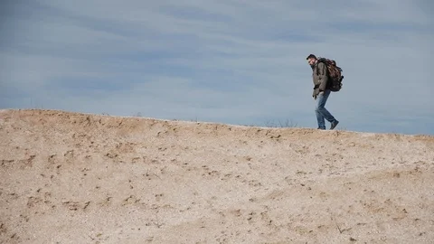 A tourist in glasses for sight with a large backpack walks along a sand mound on Stock Footage 103650453