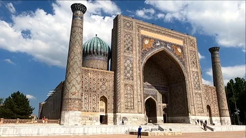 Tourist guide gesturing in front of Sher-Dor Madrasa in Samarkand Stock Footage 336913604
