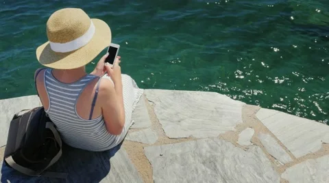 A tourist in a hat sitting on the quay, using a mobile phone. The camera moves Stock Footage 66396142