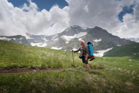 Tourist with a large backpack on the pathway in the background of high snow-c Stock Photos