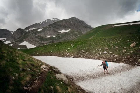 Tourist with a large backpack on the pathway in the background of high snow-c Stock Photos