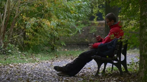 Tourist Makes a Call Sitting on the Bench in Park in Autumn Day and Talking Stock Footage 68686716