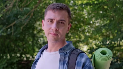 Tourist man with backpack stands in dense green forest, smiles at camera, enjoyi Stock Footage 280186382
