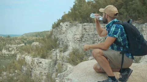 Tourist man close-up sitting the mountain drinks water. men with backpack in Stock Footage