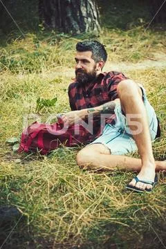 Tourist in plaid shirt hold mug. Hipster with long beard relax on green grass Stock Photos
