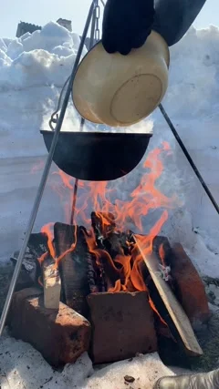 Black large tourist pot hangs over burning flame of campfire in the forest.  Cooking dinner on