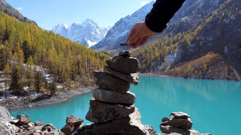Tourist put small stone on top pyramid against snow capped mountains and lake Vídeo Stock 291433362