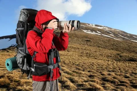 Tourist in a red jacket with a gray backpack taking pictures Stock Photos