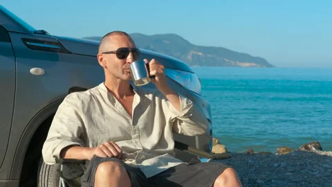 Tourist relishing a cup of coffee while seated by the serene sea Stock Footage 297607213