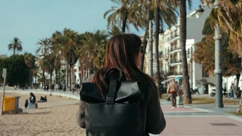 A tourist strolls along the beachfront with a backpack enjoying a sunny day. Stock Footage 332597732