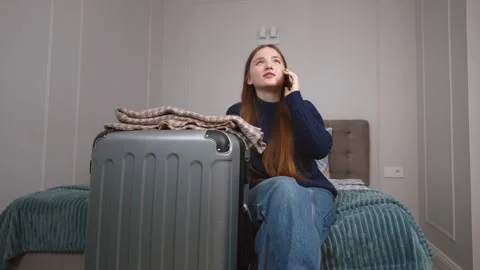 Tourist talking on phone while sitting on bed beside packed suitcase Stock Footage 309775941