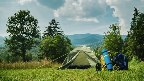 Tourist tent and two backpacks. On a beautiful green background with mountains Stock Footage